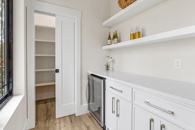 bar with wine cooler, light hardwood / wood-style flooring, and white cabinets