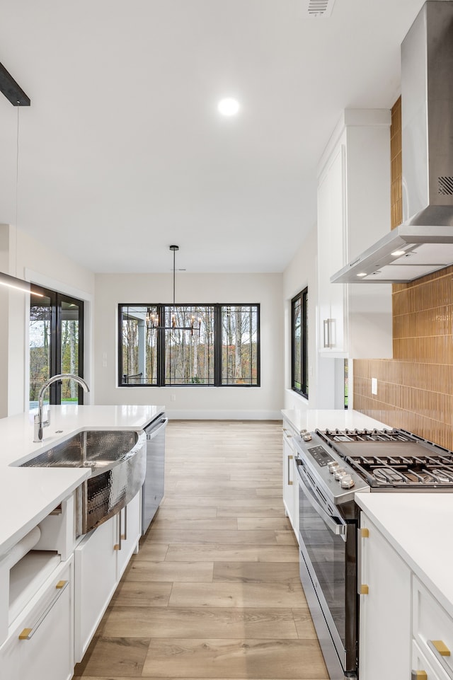 kitchen with hanging light fixtures, wall chimney range hood, backsplash, white cabinets, and appliances with stainless steel finishes