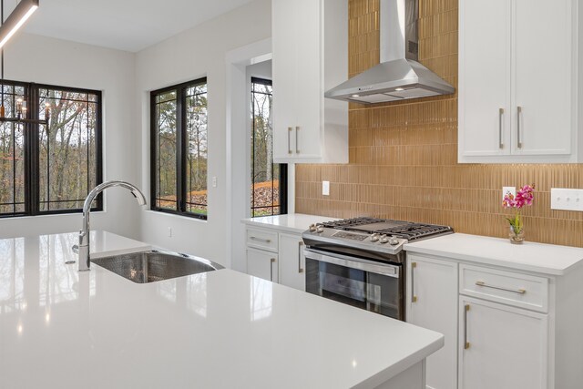 kitchen with tasteful backsplash, wall chimney exhaust hood, gas range, sink, and white cabinetry