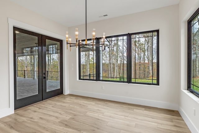 unfurnished dining area featuring french doors, light hardwood / wood-style floors, a wealth of natural light, and a notable chandelier