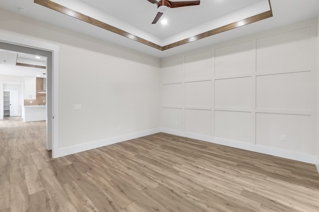 empty room featuring ceiling fan, light hardwood / wood-style floors, and a tray ceiling