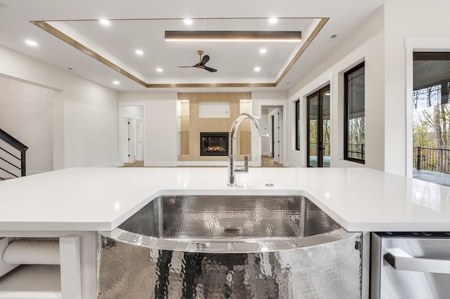 kitchen featuring a tray ceiling, a fireplace, ceiling fan, and sink