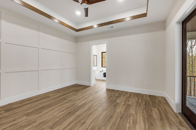 spare room with light hardwood / wood-style floors, ceiling fan, and a tray ceiling