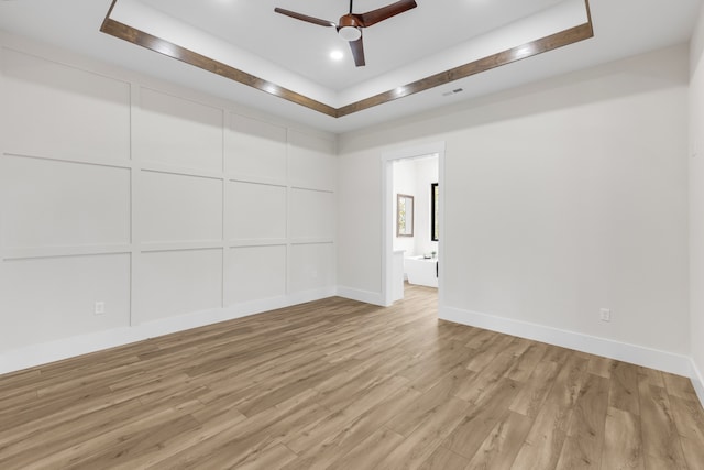 unfurnished room featuring a raised ceiling, ceiling fan, and light wood-type flooring