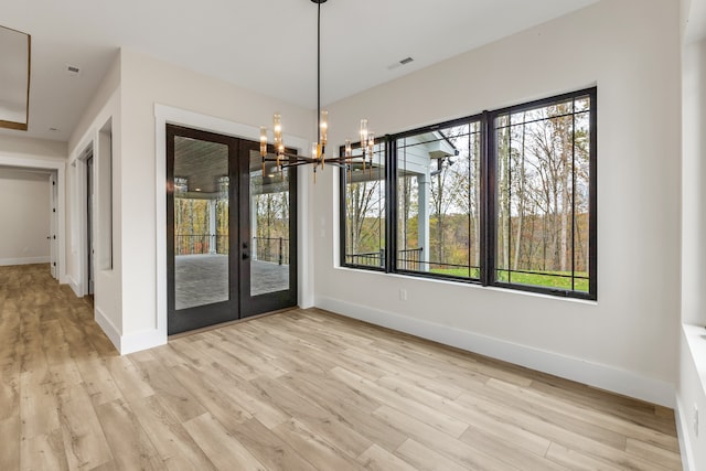 unfurnished dining area with french doors, light wood-type flooring, and a notable chandelier