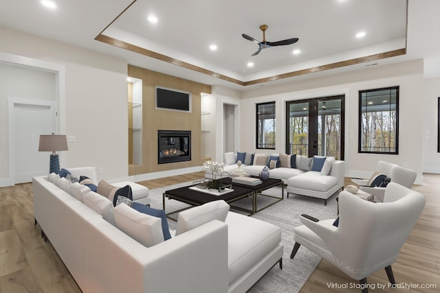 living room with a tray ceiling, ceiling fan, a fireplace, and light wood-type flooring