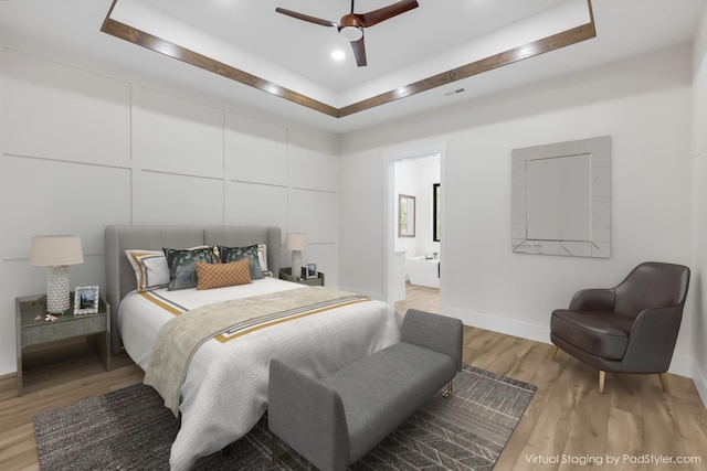 bedroom featuring light wood-type flooring, a raised ceiling, ceiling fan, and connected bathroom