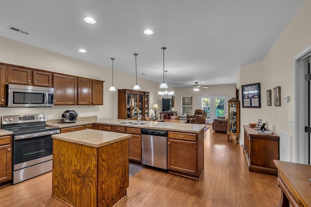 kitchen with sink, a kitchen island, kitchen peninsula, stainless steel appliances, and pendant lighting