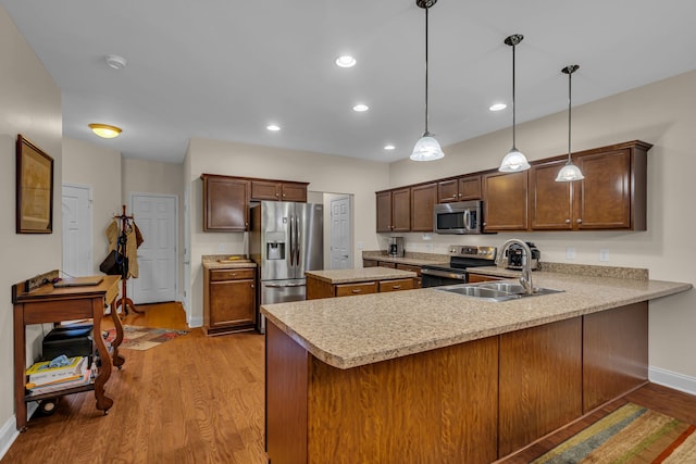 kitchen with hanging light fixtures, kitchen peninsula, stainless steel appliances, sink, and light hardwood / wood-style floors