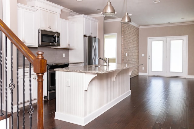 kitchen with a kitchen bar, an island with sink, stainless steel appliances, white cabinets, and light stone counters