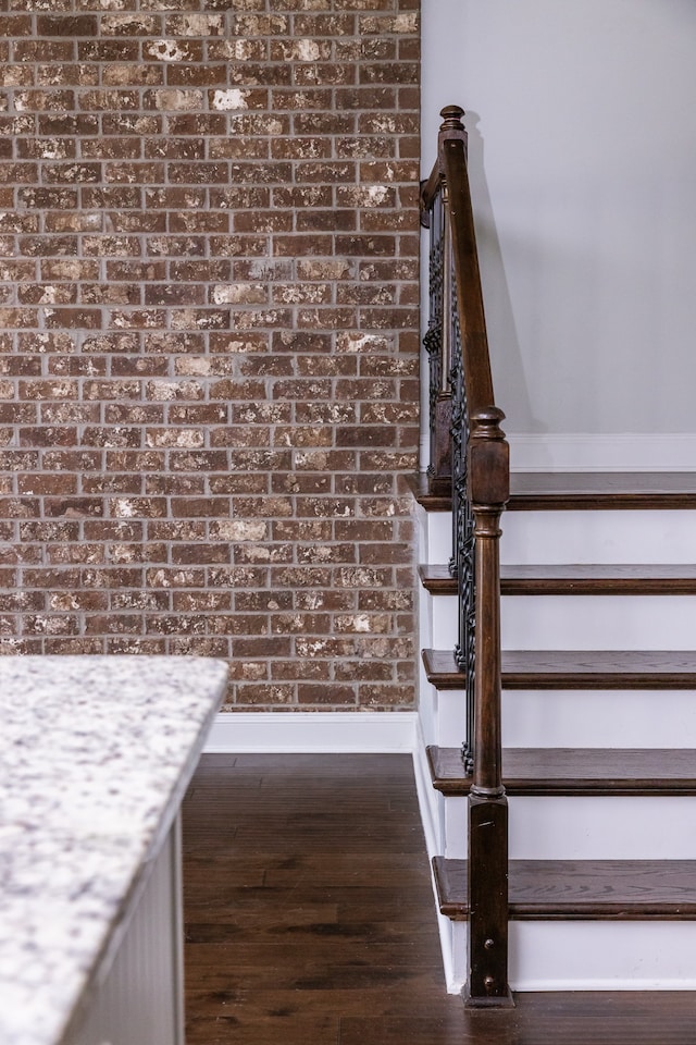 stairs featuring brick wall and hardwood / wood-style floors