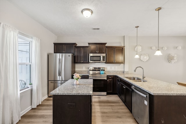 kitchen featuring dark brown cabinets, hanging light fixtures, light hardwood / wood-style flooring, sink, and stainless steel appliances