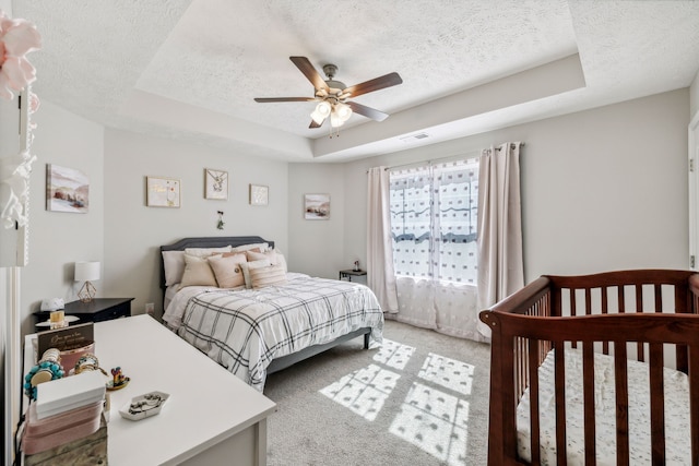 carpeted bedroom featuring ceiling fan, a raised ceiling, and a textured ceiling