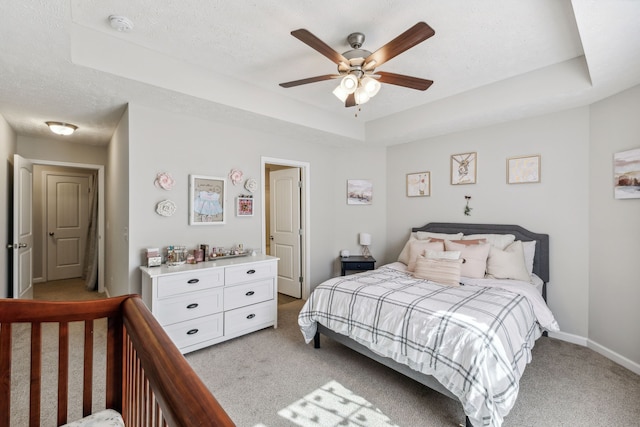 bedroom with ceiling fan, light carpet, a textured ceiling, and a tray ceiling