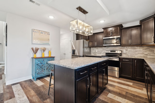 kitchen with hanging light fixtures, stainless steel appliances, backsplash, hardwood / wood-style floors, and a center island