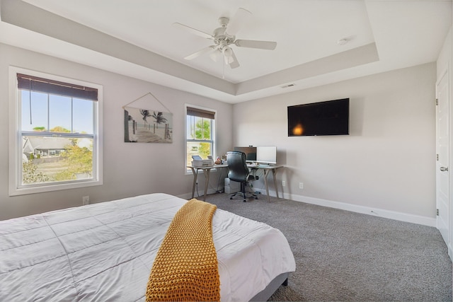 carpeted bedroom with a raised ceiling and ceiling fan