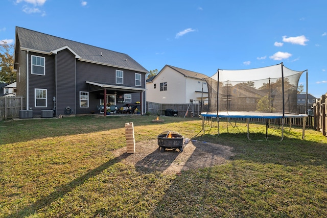 rear view of house with central AC, a lawn, a trampoline, and a fire pit