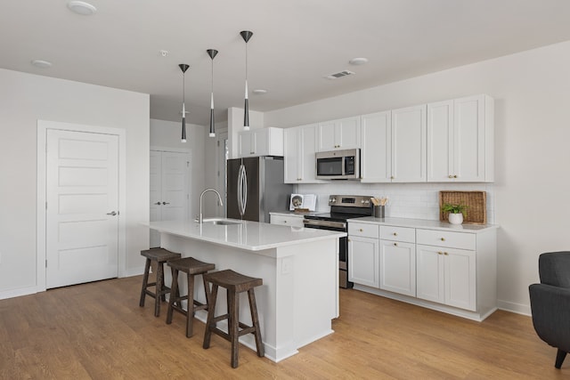 kitchen with hanging light fixtures, a center island with sink, appliances with stainless steel finishes, white cabinetry, and sink