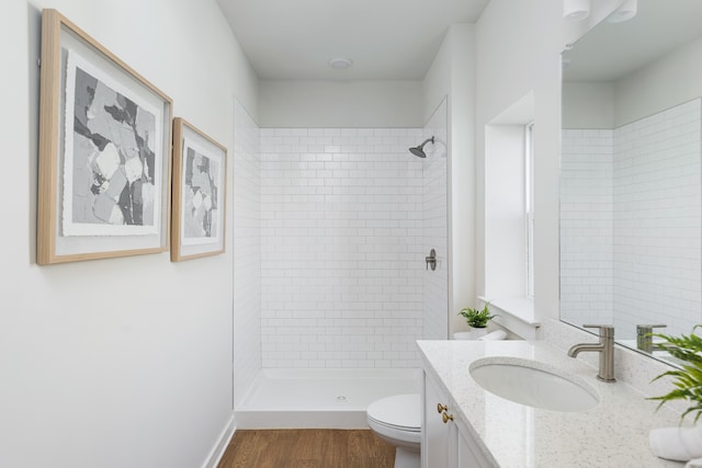 bathroom featuring vanity, hardwood / wood-style floors, a tile shower, and toilet