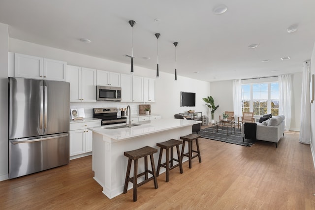 kitchen featuring an island with sink, stainless steel appliances, sink, decorative light fixtures, and white cabinets