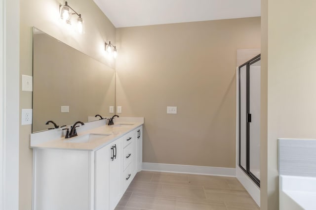 full bath featuring baseboards, a sink, a shower stall, and double vanity