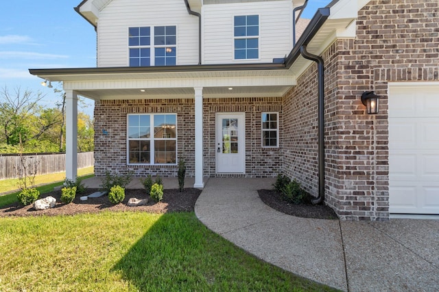 entrance to property with brick siding, a yard, a garage, and fence