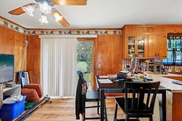 dining area with crown molding, wood walls, light wood-type flooring, and ceiling fan