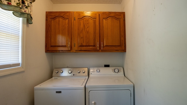 clothes washing area with washer and dryer, a textured ceiling, and cabinets