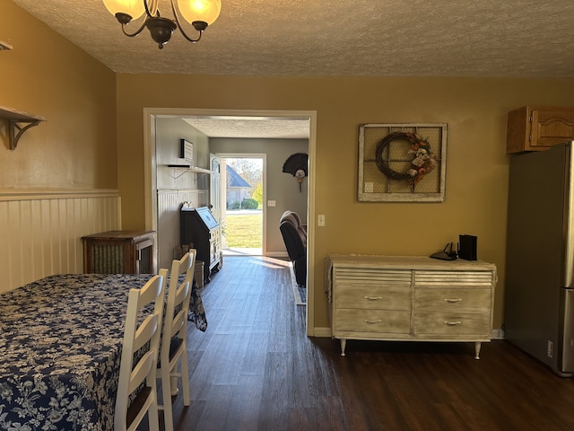 bedroom with a textured ceiling, access to exterior, dark wood-type flooring, a notable chandelier, and stainless steel refrigerator