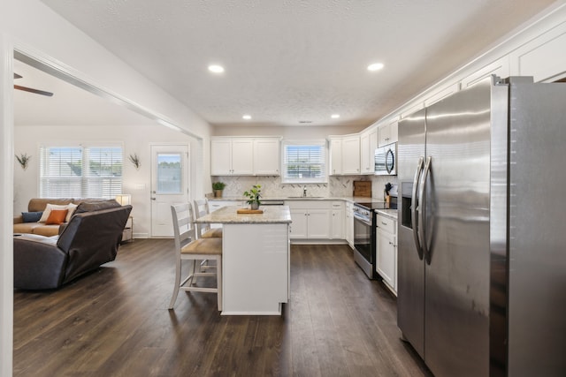 kitchen with a kitchen island, a kitchen bar, white cabinetry, appliances with stainless steel finishes, and dark hardwood / wood-style flooring