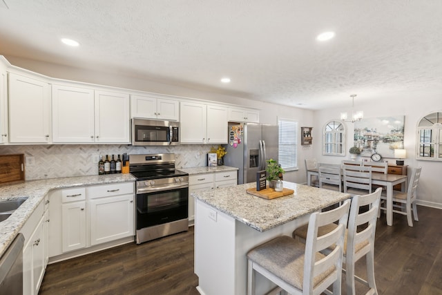 kitchen featuring white cabinets, hanging light fixtures, light stone counters, dark hardwood / wood-style floors, and stainless steel appliances