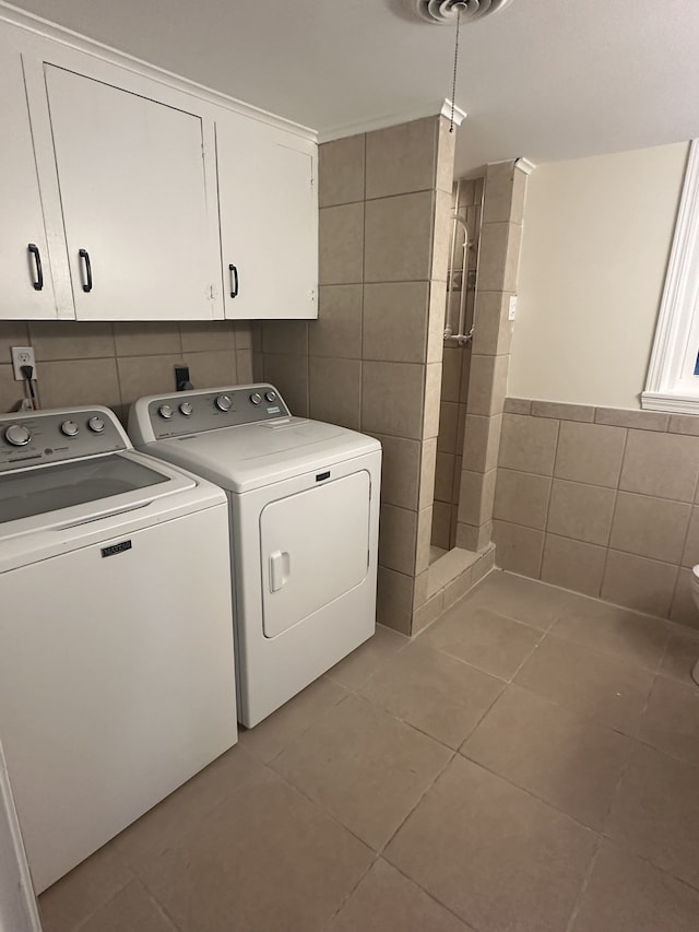 laundry area featuring tile walls, light tile patterned floors, washing machine and clothes dryer, and cabinets