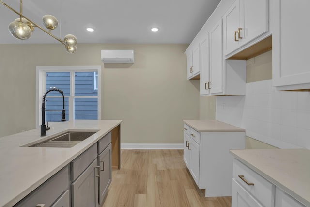 kitchen with a wall mounted AC, pendant lighting, light wood-type flooring, white cabinetry, and sink