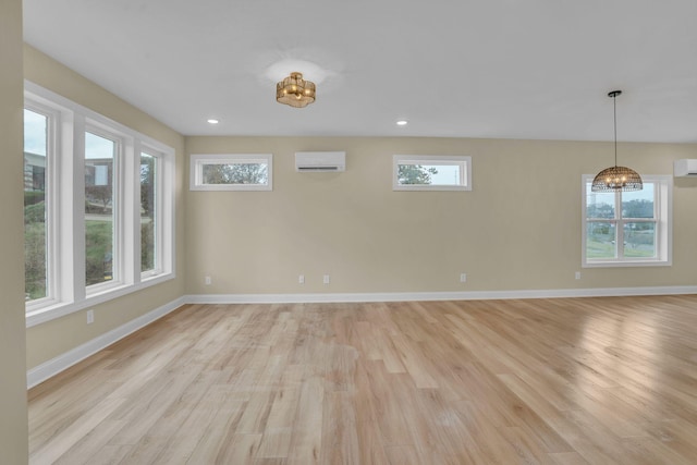 empty room with an inviting chandelier, a wall unit AC, and light hardwood / wood-style flooring