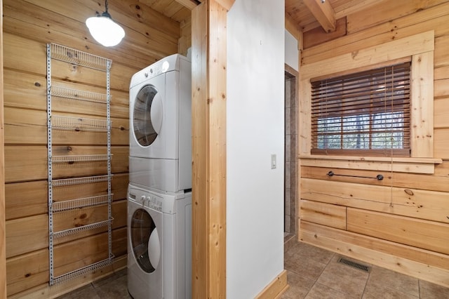 laundry area with stacked washer and dryer, tile patterned flooring, and wood walls