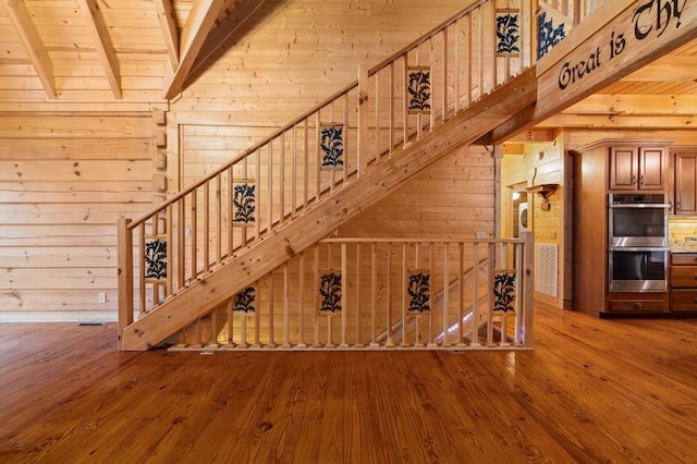 unfurnished living room featuring wood ceiling, a high ceiling, wood-type flooring, beamed ceiling, and wood walls