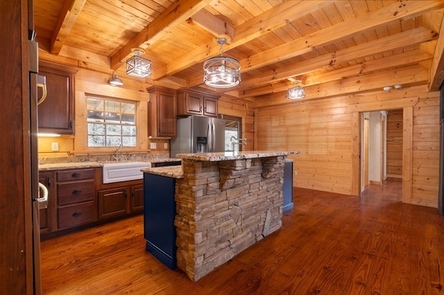 kitchen with decorative light fixtures, sink, light stone counters, stainless steel fridge with ice dispenser, and a center island with sink