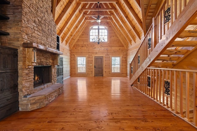 unfurnished living room featuring high vaulted ceiling, wooden walls, beamed ceiling, a fireplace, and hardwood / wood-style floors