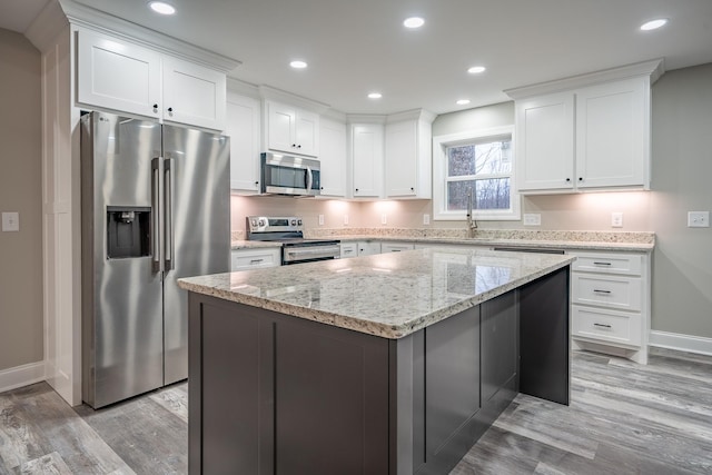 kitchen featuring light stone counters, light wood finished floors, a kitchen island, stainless steel appliances, and white cabinets