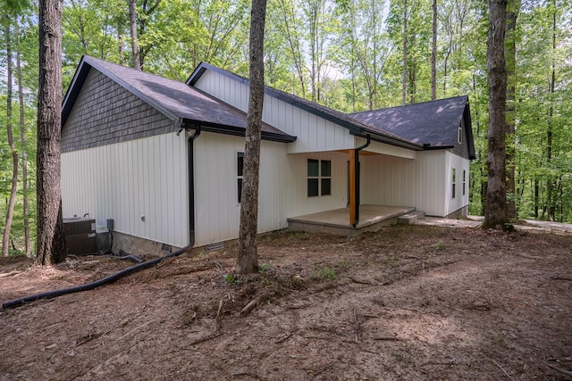 view of side of property with central AC unit and roof with shingles