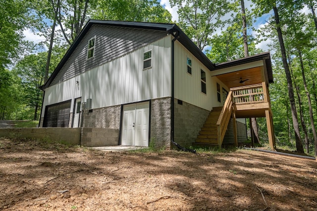 back of house featuring a garage, ceiling fan, dirt driveway, and stairway