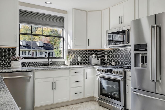 kitchen with a sink, marble finish floor, white cabinets, appliances with stainless steel finishes, and light stone countertops