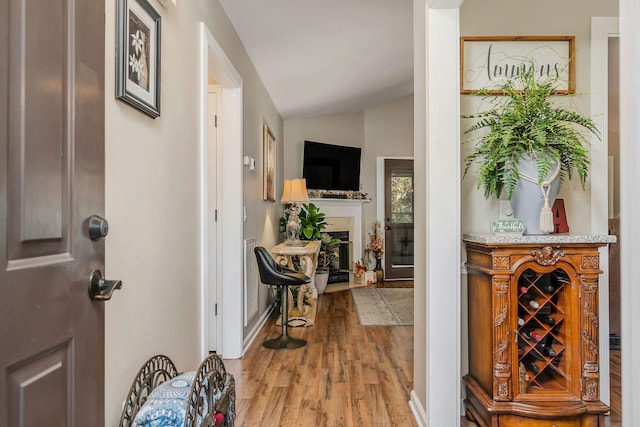 foyer entrance with lofted ceiling, baseboards, light wood-style floors, and a fireplace with raised hearth