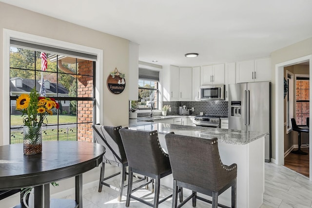 kitchen featuring tasteful backsplash, white cabinets, baseboards, appliances with stainless steel finishes, and light stone countertops