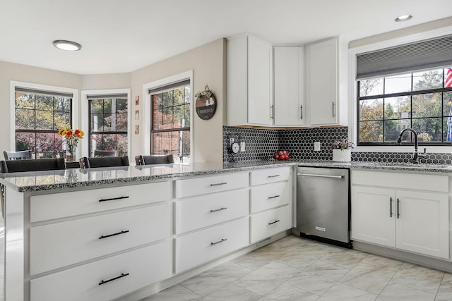 kitchen with a peninsula, dishwasher, marble finish floor, and light stone counters