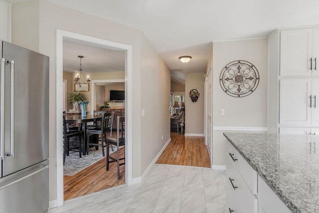 interior space featuring high end refrigerator, light stone counters, marble finish floor, white cabinets, and a notable chandelier