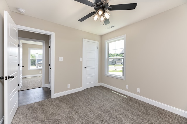 unfurnished bedroom featuring multiple windows, dark carpet, and ceiling fan