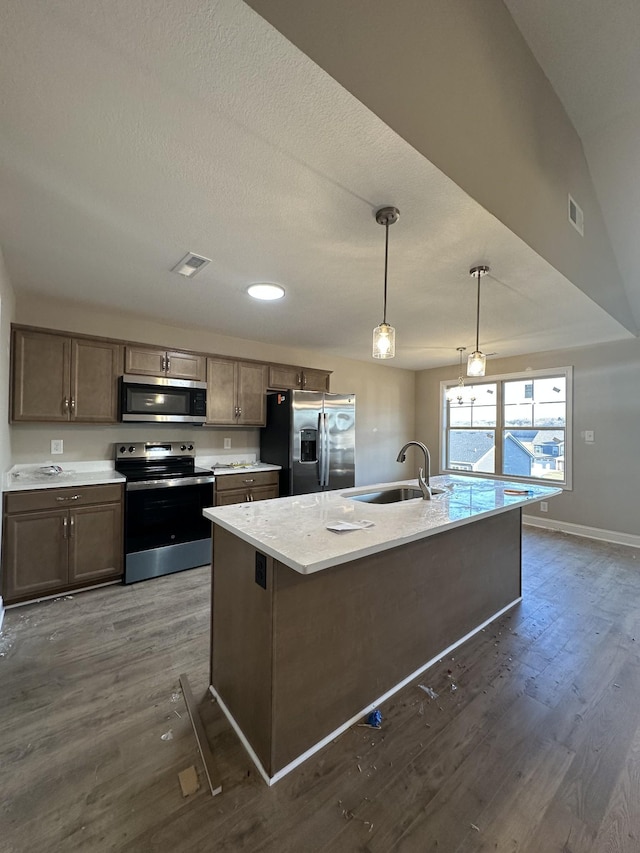 kitchen with pendant lighting, sink, stainless steel appliances, a center island with sink, and dark hardwood / wood-style flooring