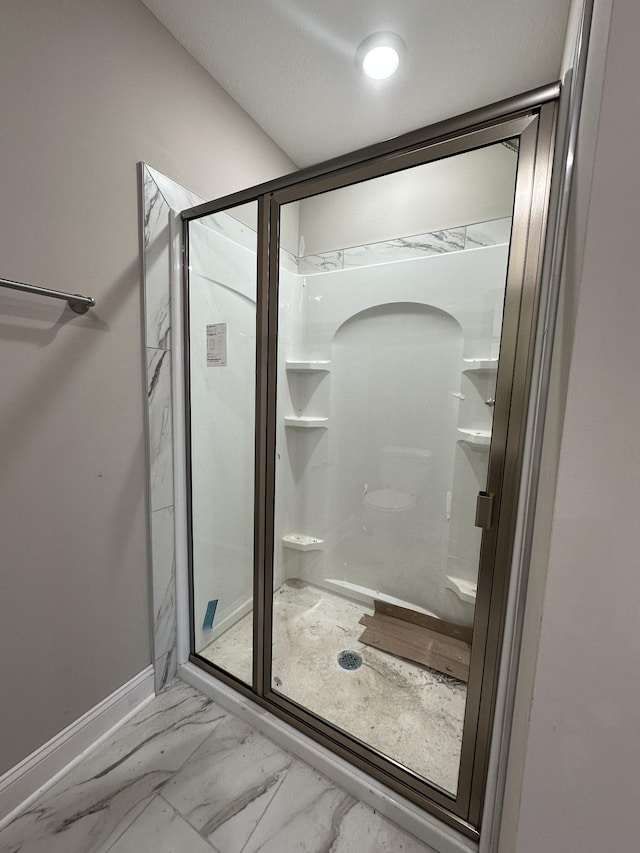 bathroom with marble finish floor, a stall shower, and baseboards