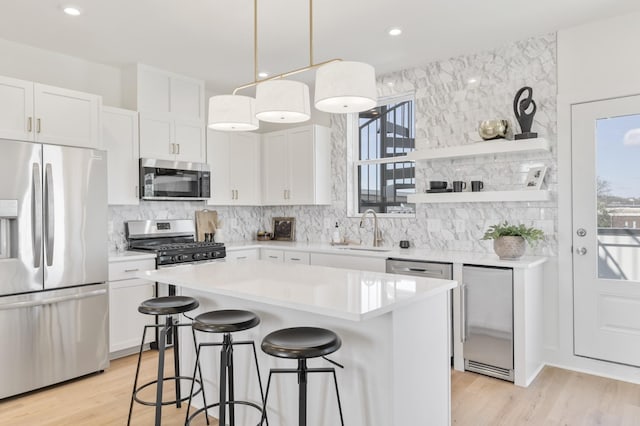 kitchen with appliances with stainless steel finishes, pendant lighting, white cabinetry, sink, and a center island